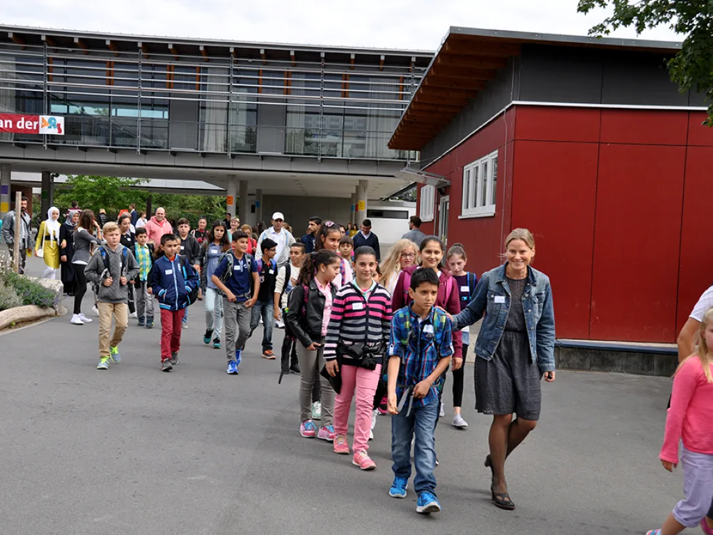 Eine Lehrkraft führt eine Gruppe Kinder über den Schulhof.